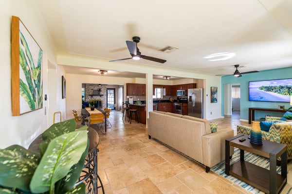 Open-plan living room with beige sofa, dining area, kitchen with dark wood cabinets, and turquoise accent wall with TV
