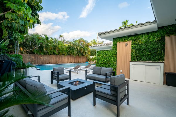 Backyard with fire pit, lounge chairs, cornhole game, and two-story white house with wooden deck