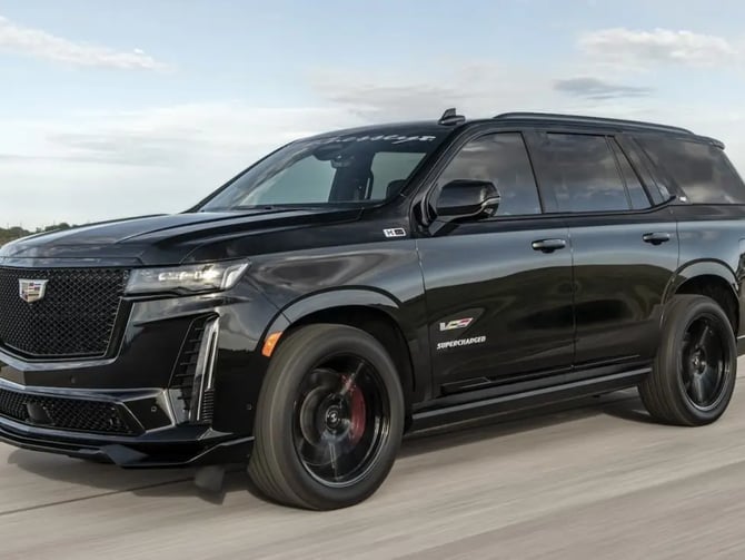 Black luxury SUV driving on a straight road with flat grassland and sky in background