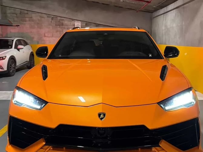 Bright orange sports car parked in concrete garage with white and yellow vehicles nearby