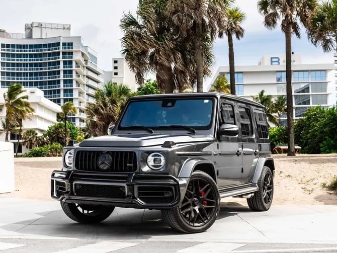 Black SUV parked on beach promenade with palm trees and beachfront hotels in background